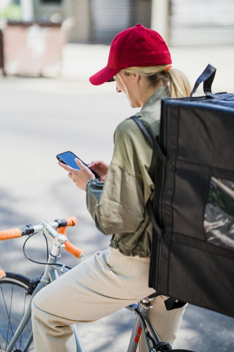A bicycle courier checks her phone while making a delivery in an urban setting.